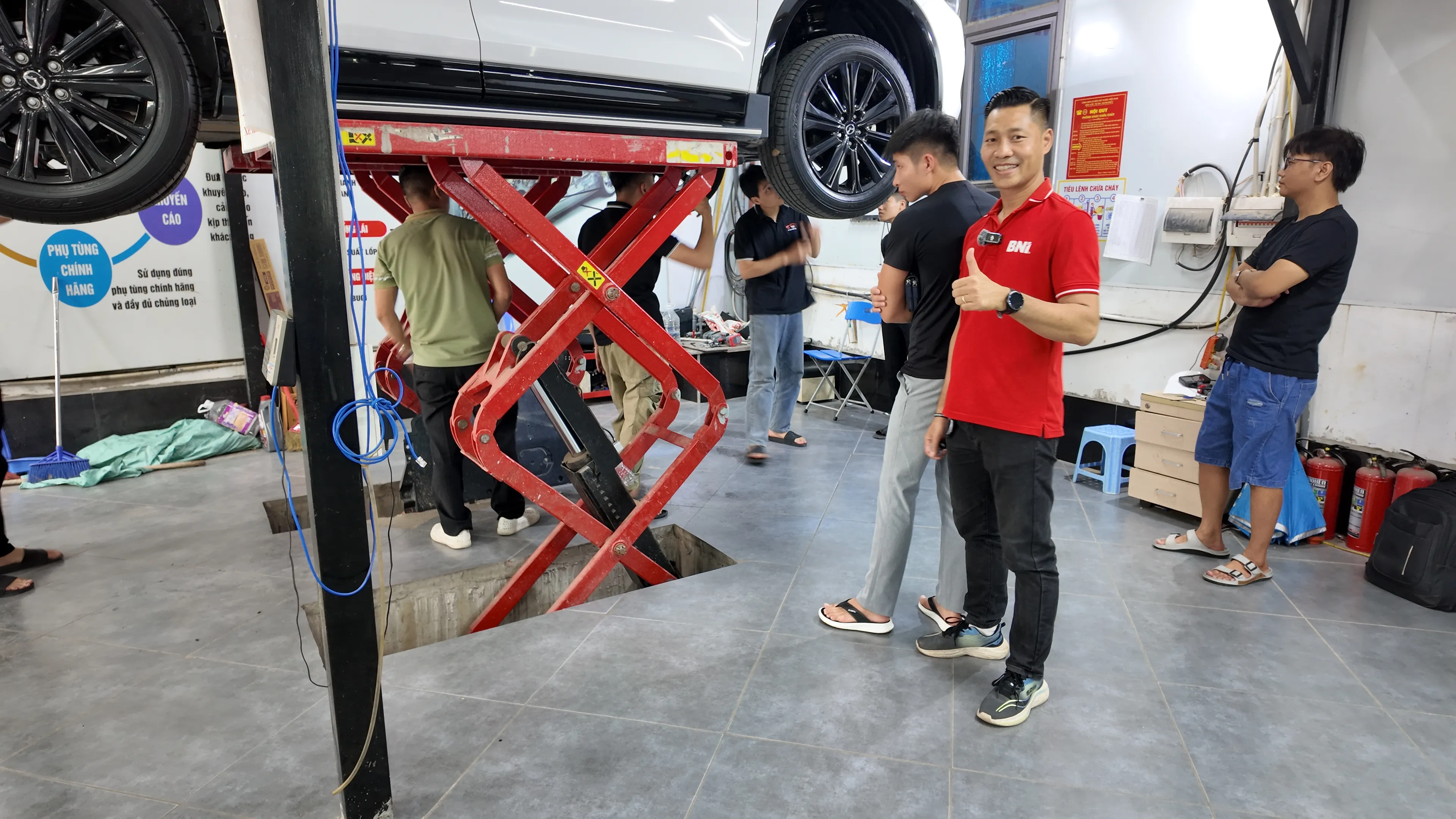 Trương Văn Trung trong áo đỏ BNI tại garage thẩm định xe — kết hợp công việc thẩm định kỹ thuật với mạng lưới doanh nhân BNI